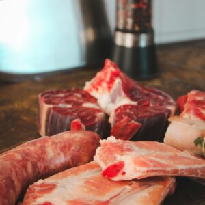 Various cuts of raw meat on a rustic kitchen table with a pepper grinder in the background.